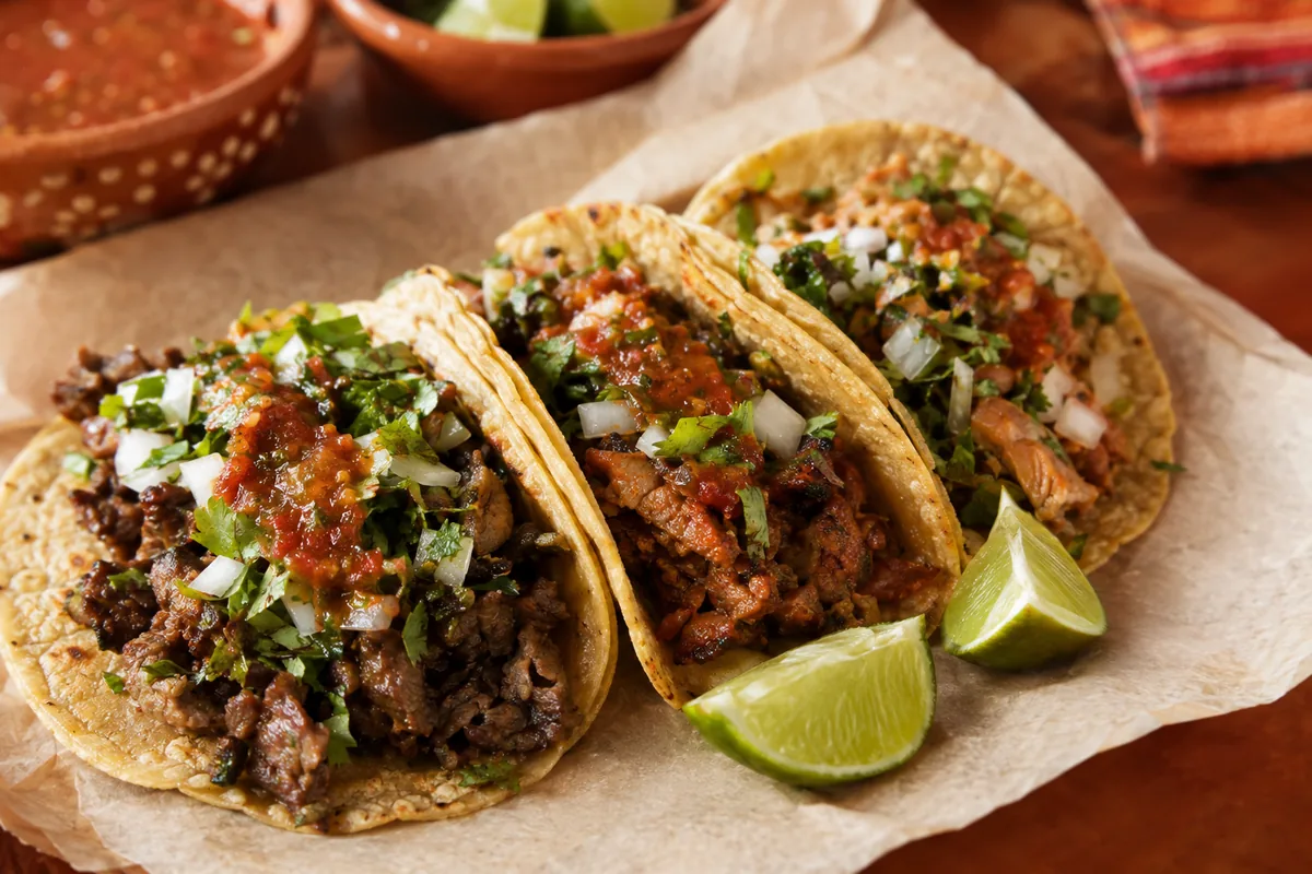 Tacos mexicanos en tortillas de maíz con cilantro, cebolla, salsa roja y limón